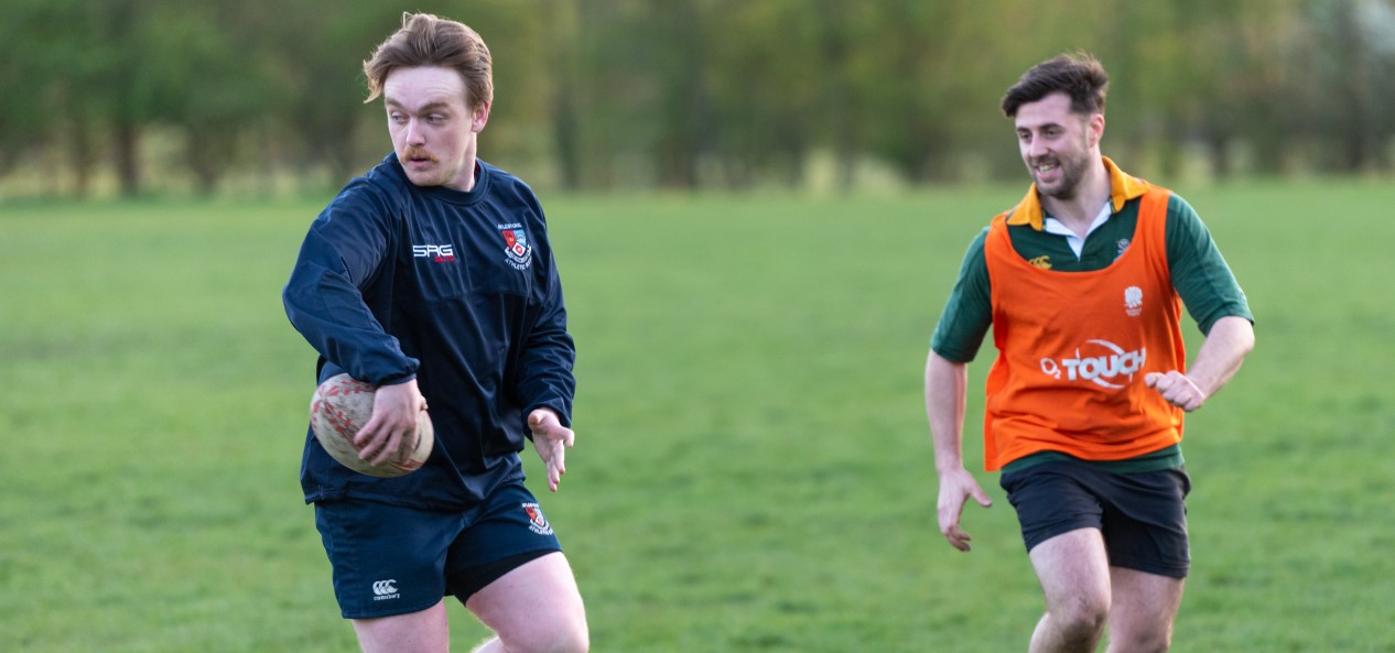 A rugby player looks to offload the ball as his opponent closes in.