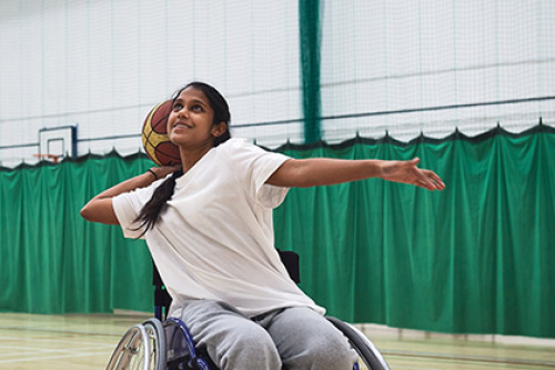 A South Asian young female shoots at the basket while playing wheelchair basketball in a sports hall