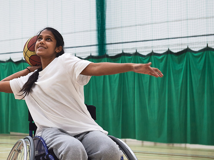 A South Asian young female shoots at the basket while playing wheelchair basketball in a sports hall