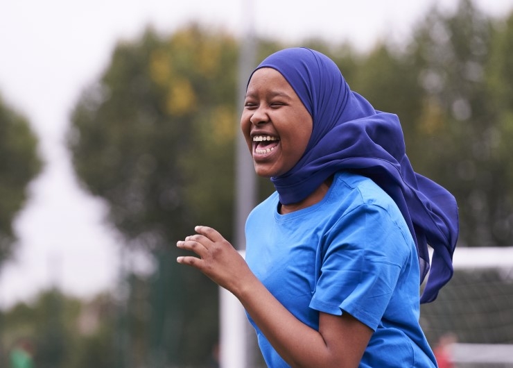 A girl laughs on an outdoor football pitch.
