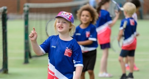 Young children playing tennis outdoors.