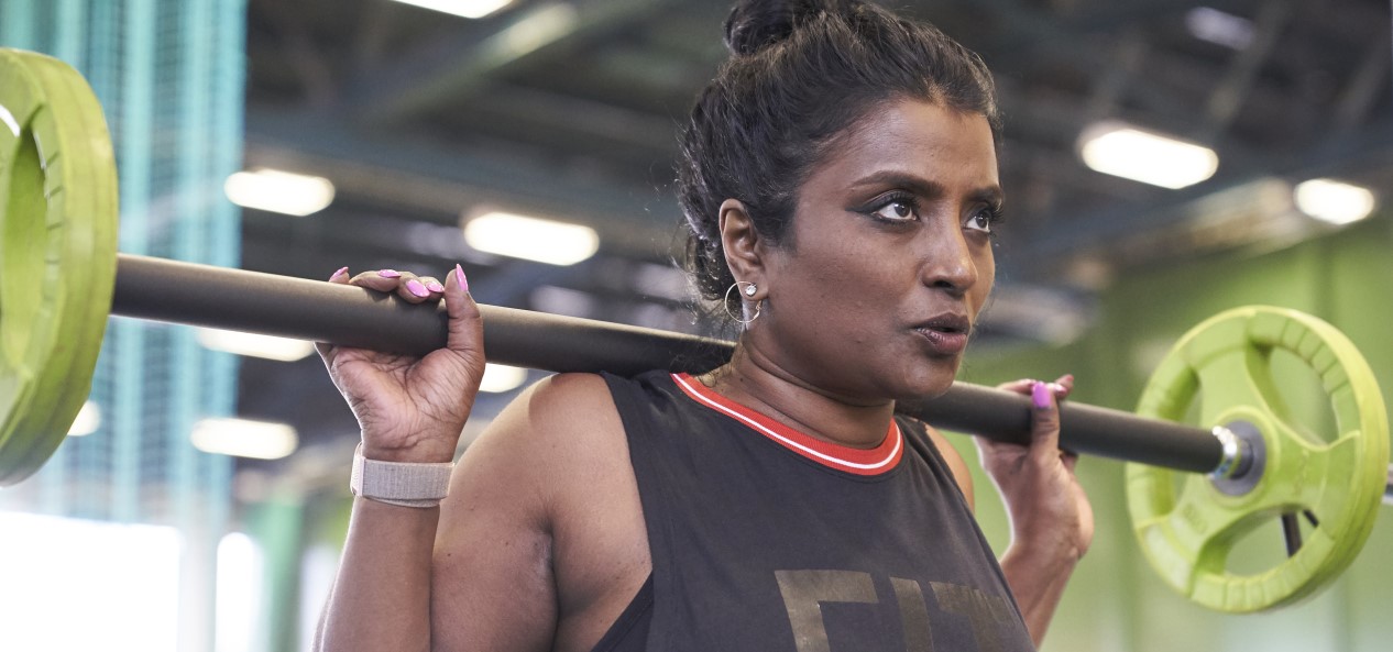 A woman holds a barbell above her shoulders in a gym.