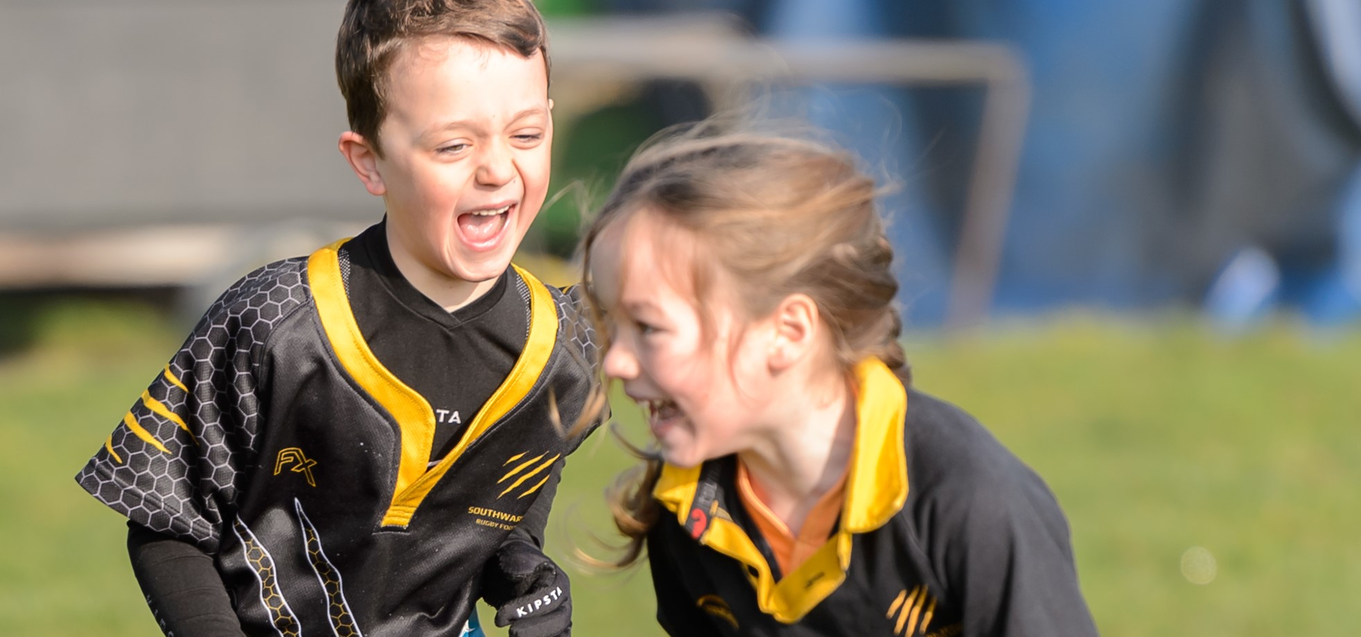 A young boy chases a girl during a game of tag rugby, with both players sporting wide smiles.