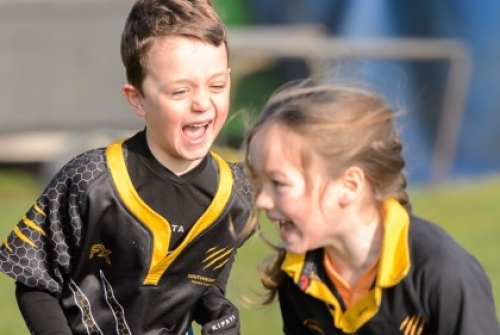 A young boy chases a girl during a game of tag rugby, with both players sporting wide smiles.