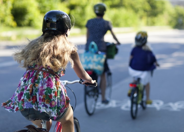 A mother and two young children, all wearing helmets, ride on a cycle path.