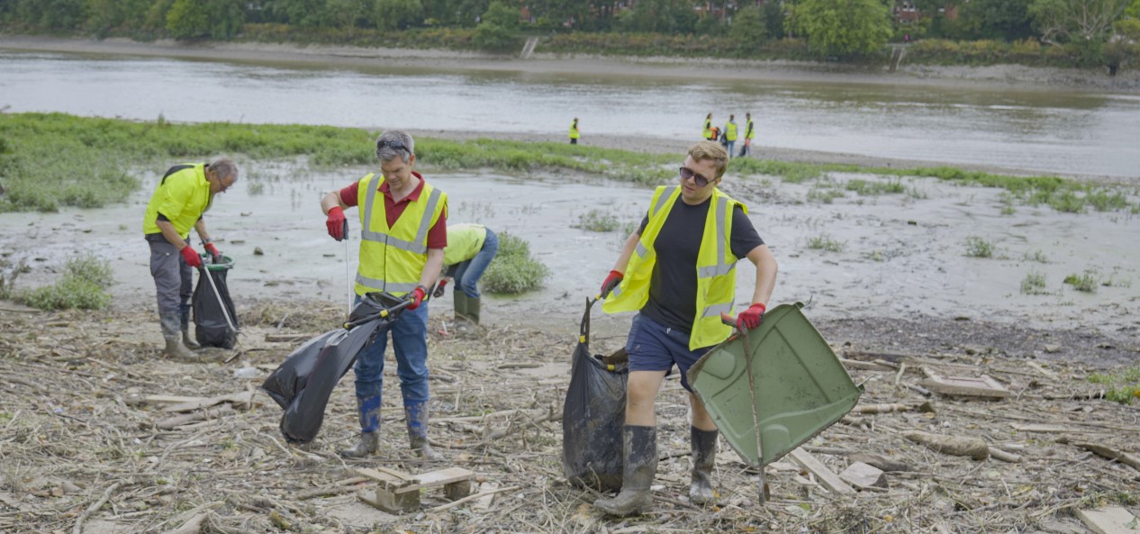 Three people wearing high-vis vests pick litter from the banks of the River Thames.