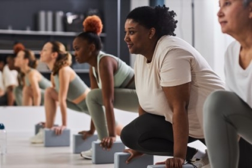 A row of women lunging with blocks in a fitness class.