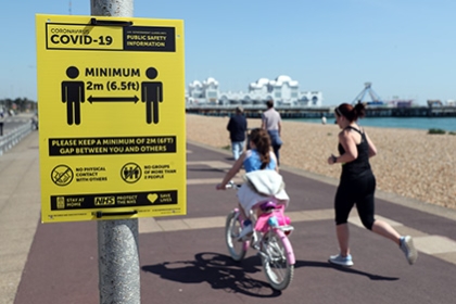 People exercise along Southsea seafront, running and riding past a sign warning about social distancing.