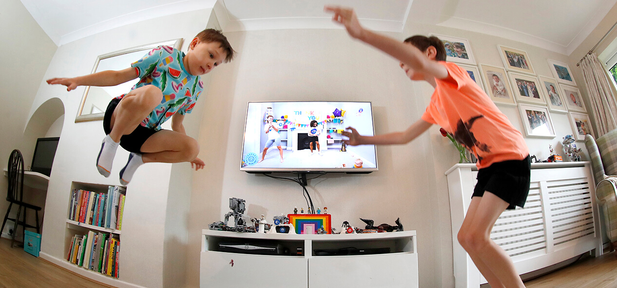 Two boys jump while the television is on in their living room.