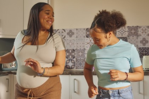 A pregnant woman and a girl dance in a kitchen.