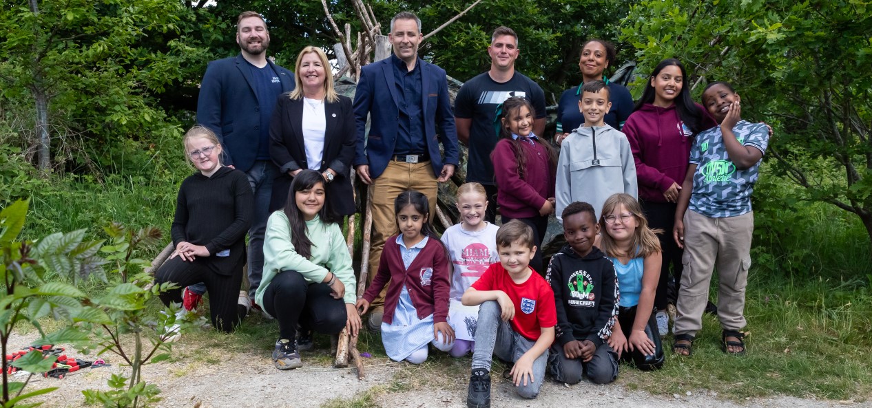 A group of children and adults, including Lisa Dodd-Mayne, Sport England's executive director of place, pose for a group picture outdoors in Bradford.