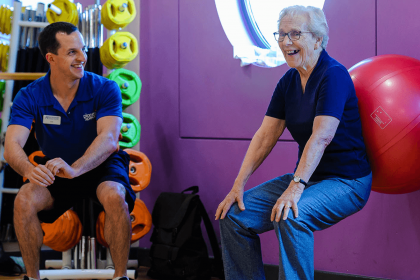 Elderly lady using exercise ball with coach