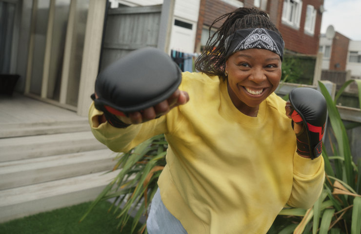 A smiling woman wearing boxing gloves in a back garden.