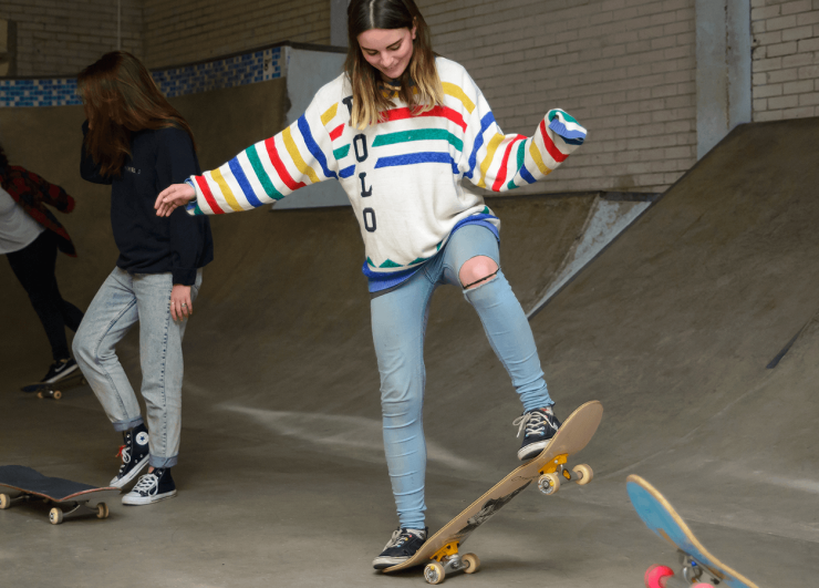 Young woman learning to ride skate board in skate park.